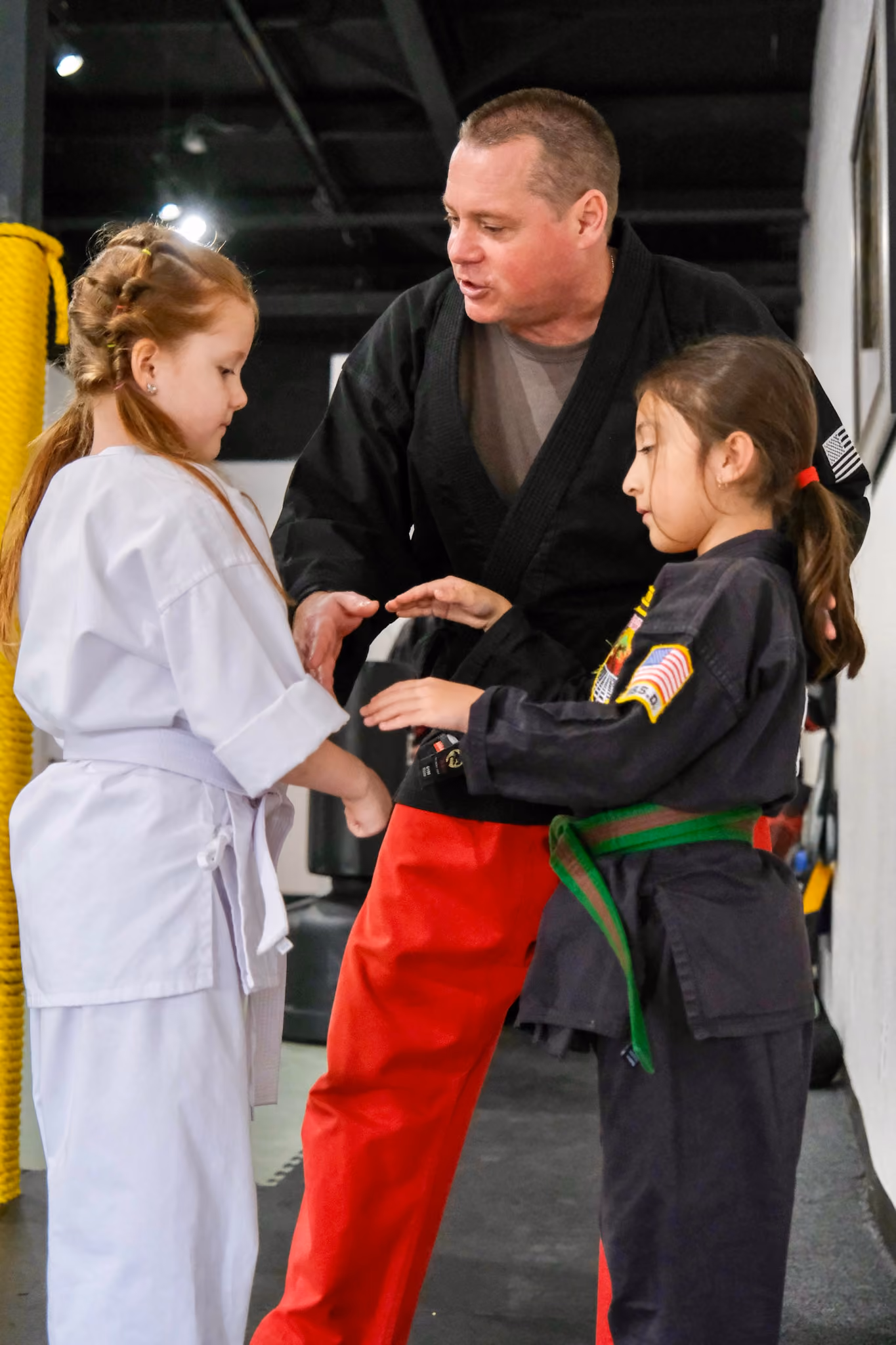 Martial arts instructor guiding two young girls in white and black uniforms during a class.