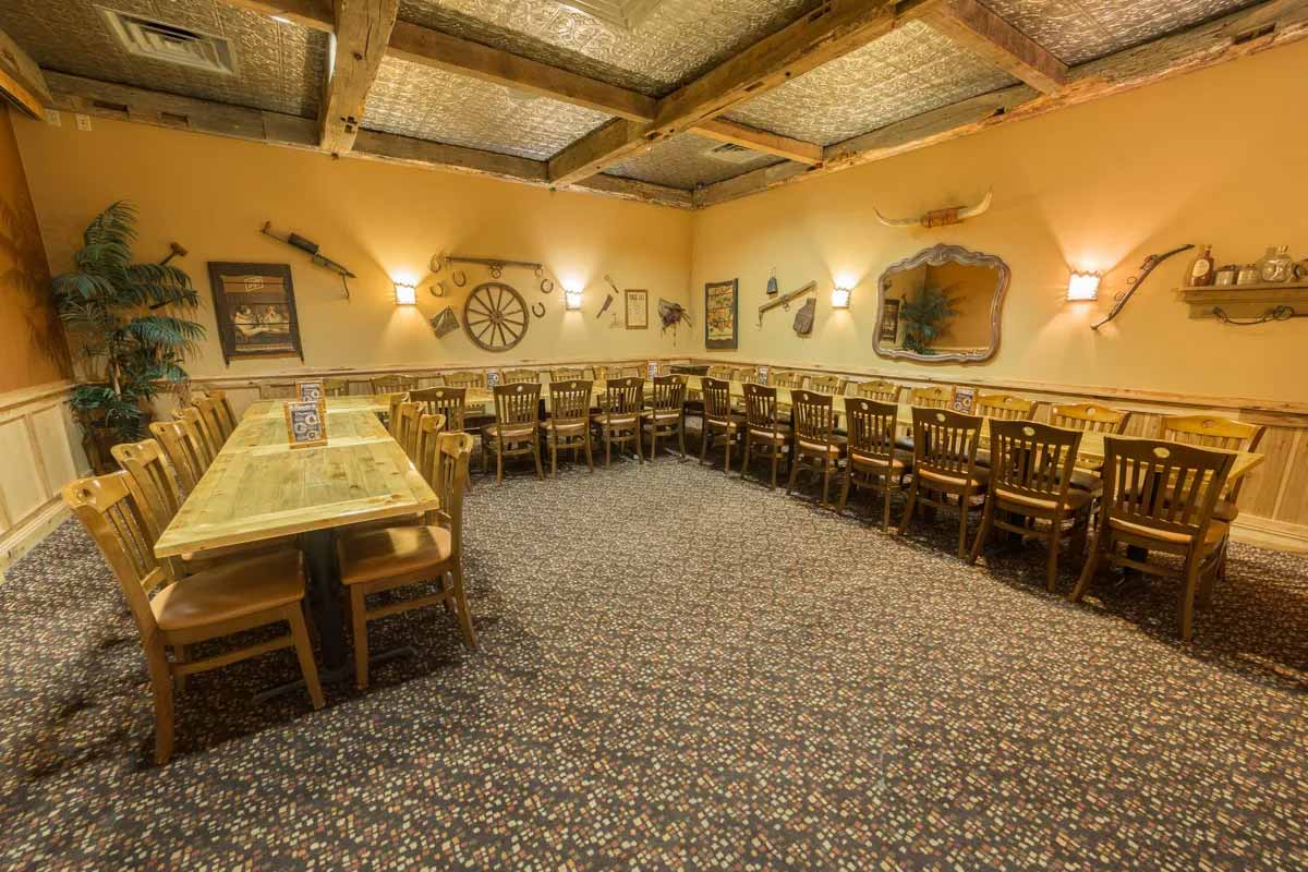 Large dining room with wooden chairs and tables arranged in a U-shape, decorated with western-themed wall items and warm lighting.