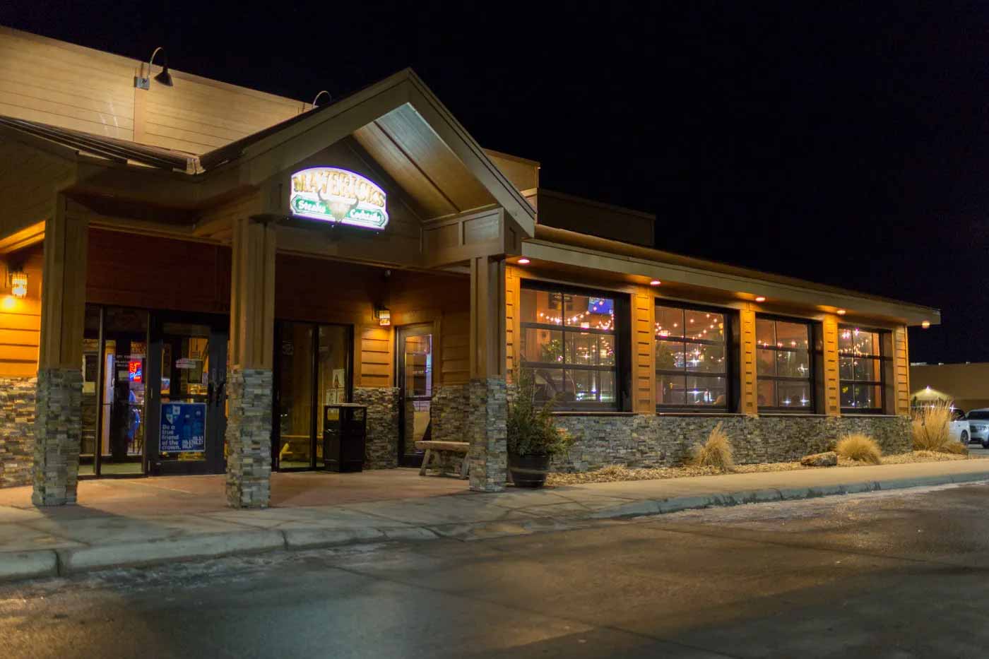 Exterior of a restaurant at night with warm lighting and large windows showing string lights inside.