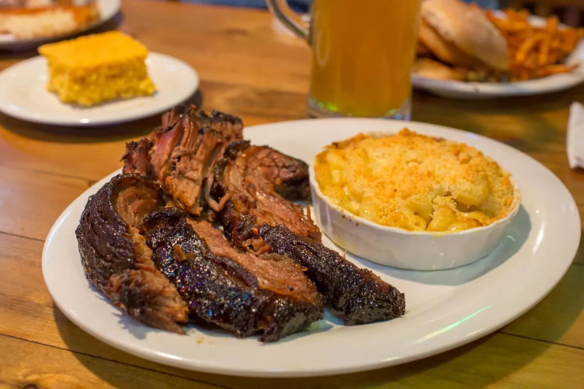 Plate with sliced smoked brisket and a side of baked macaroni and cheese with a crumb topping.