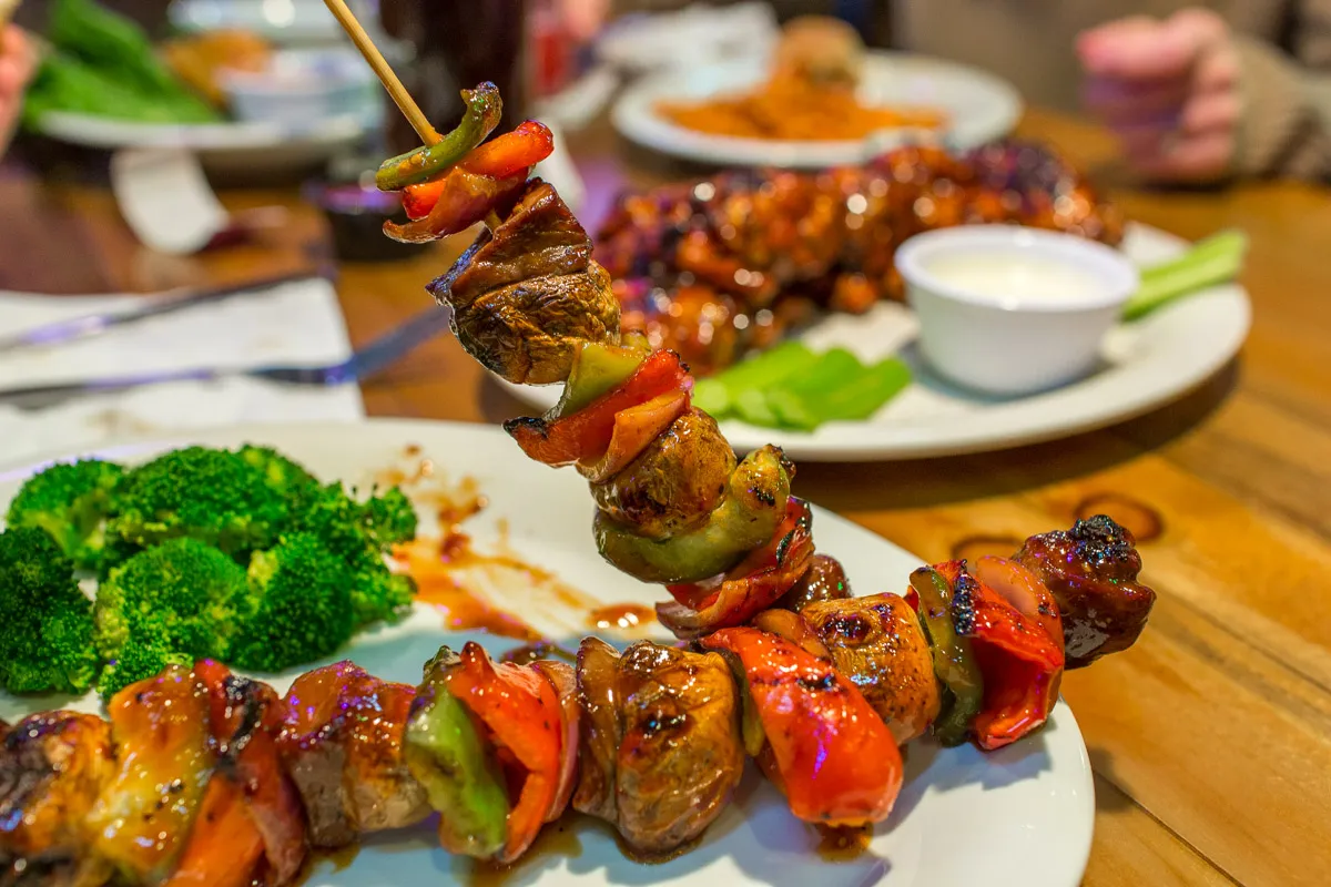 Grilled vegetable and meat skewers served with steamed broccoli on a white plate.