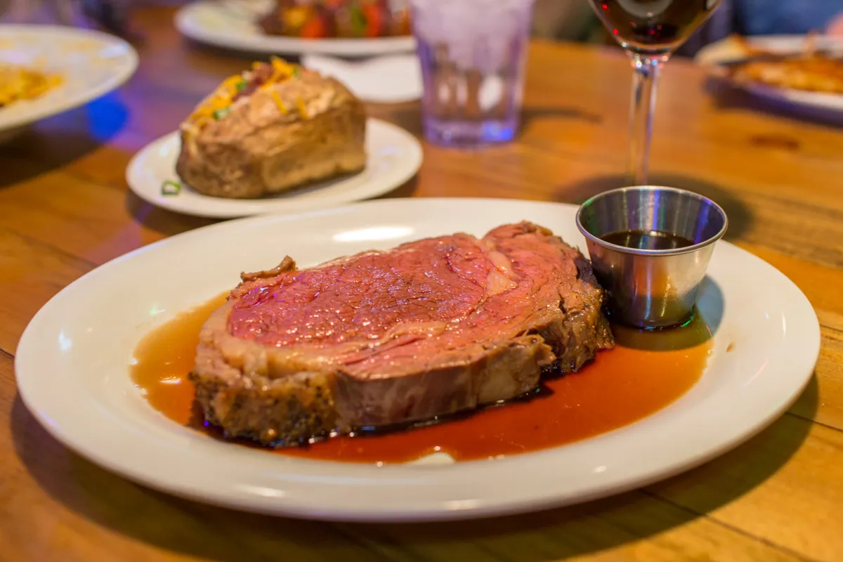 Juicy slice of rare prime rib served with au jus sauce and a small cup of dipping sauce on a white plate.