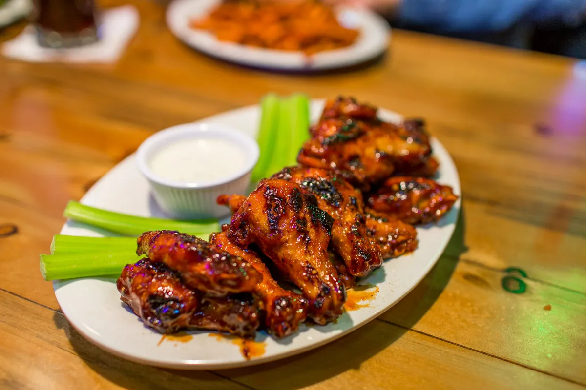 Plate of glazed chicken wings with celery sticks and a cup of ranch dressing on a wooden table.