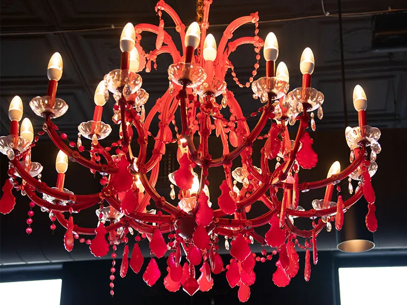 Ornate red chandelier with multiple lit candle-shaped bulbs hanging from a ceiling.