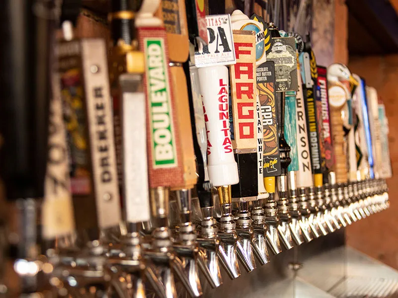 Row of beer tap handles with various brand labels in a bar setting.