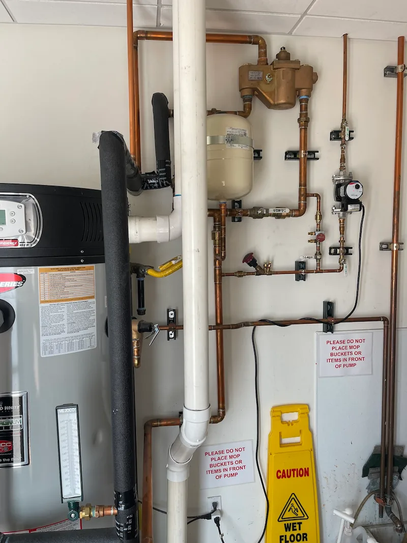 Water heater and complex copper piping with caution signs against placing items in front of the pump.
