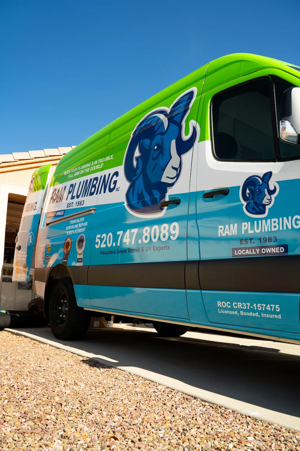 Side view of a Ram Plumbing service van with logo, phone number, and service details in green, blue, and white.