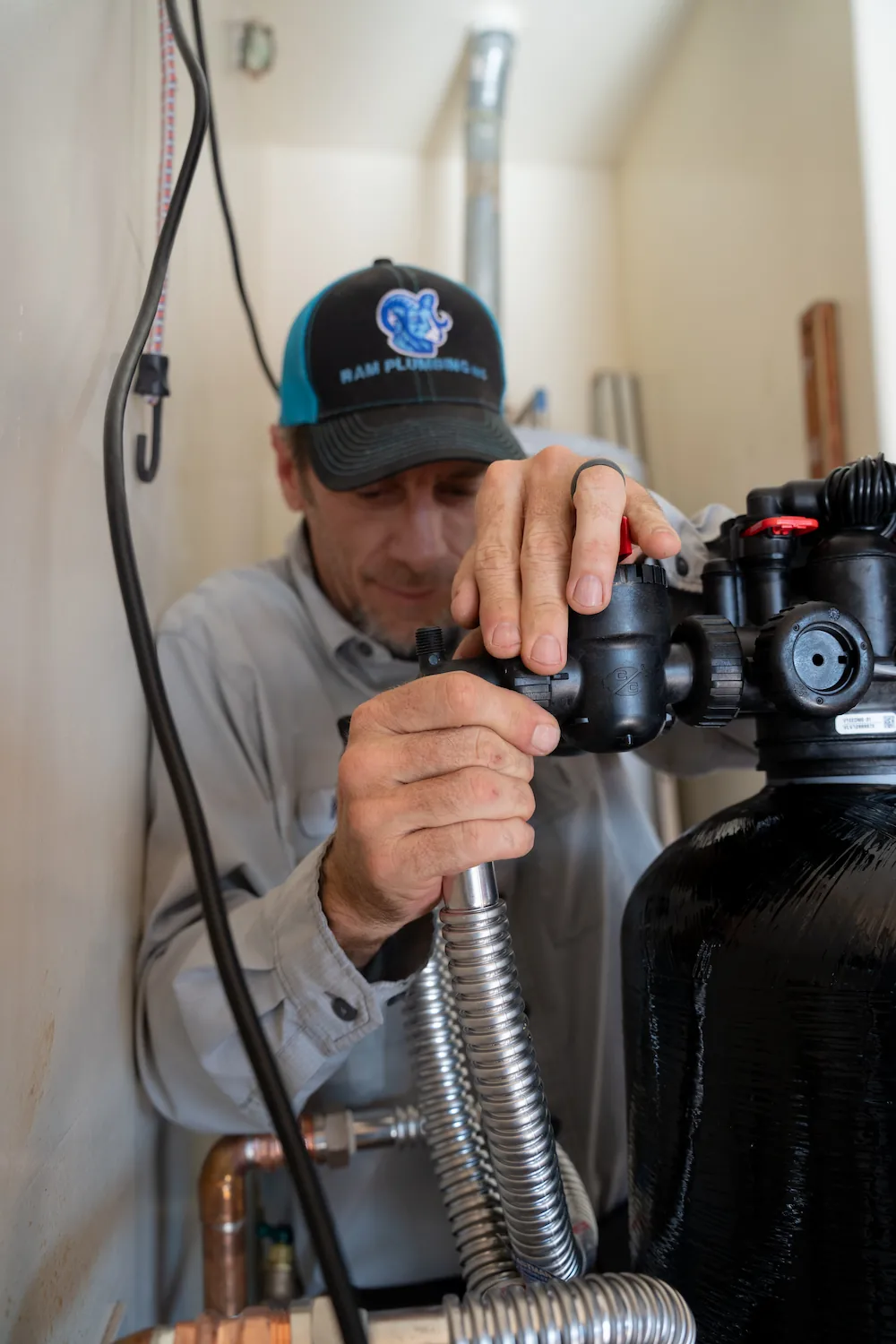 Plumber in Ram Plumbing cap adjusting valves on water filtration system pipes.