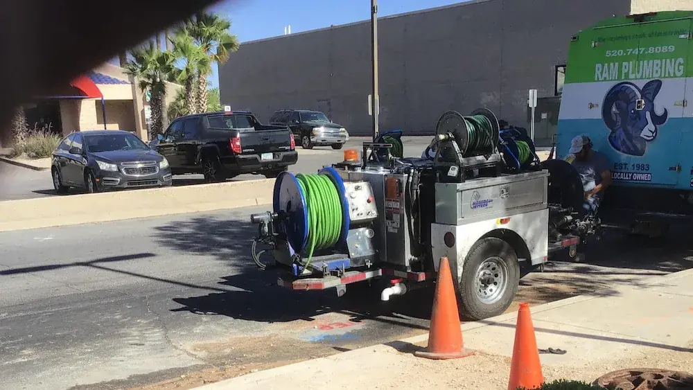 Plumbing service trailer with hose reels parked near orange safety cones on street during daytime.