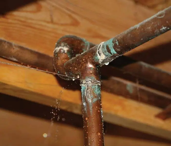 Close-up of corroded copper pipes with water droplets on wooden ceiling background.