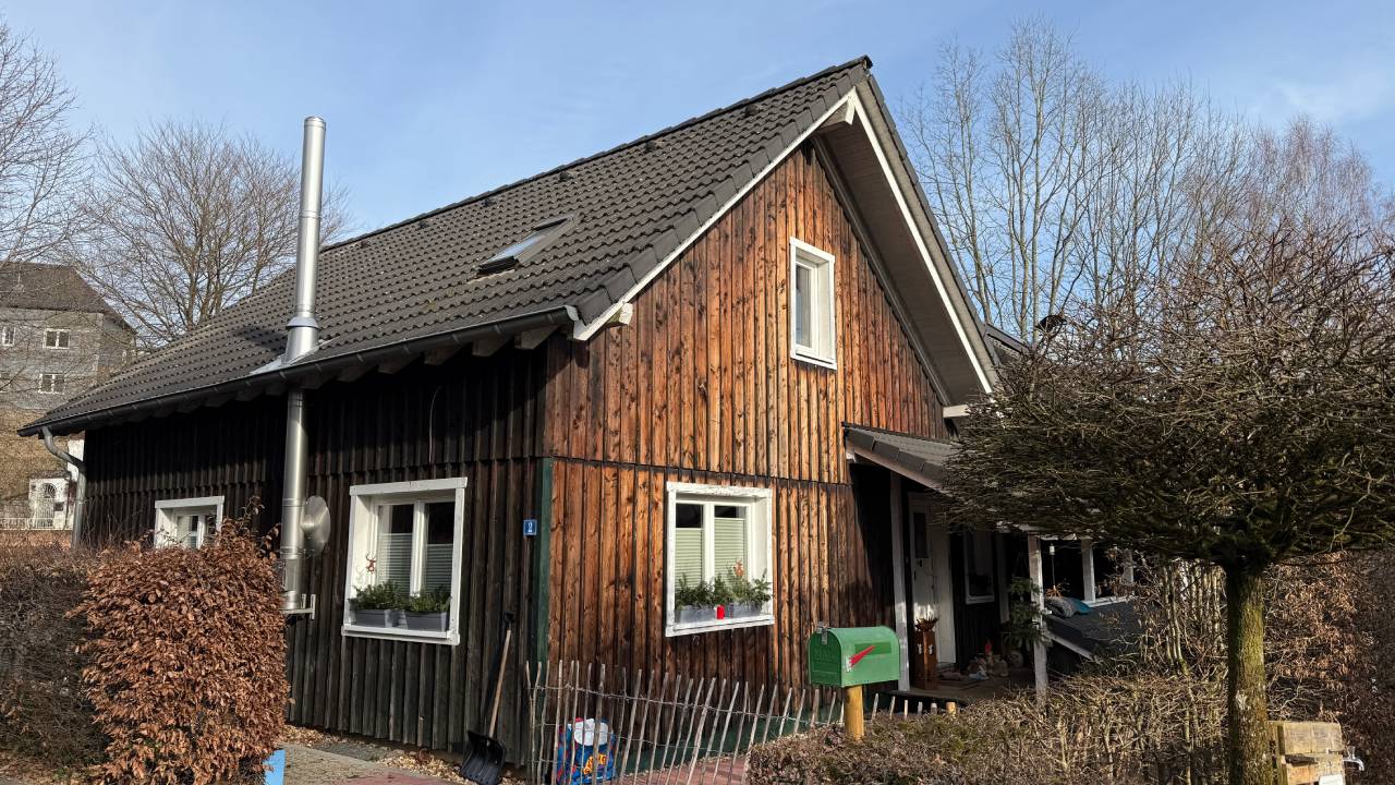 Modernes weißes Haus mit großen Fenstern, Glasbalkonen, Terrasse und Garten mit Baum.