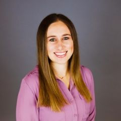 Smiling young woman with long brown hair wearing pink button-up shirt