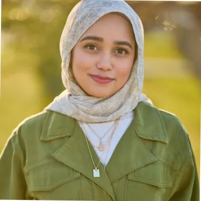 Young woman wearing beige headscarf and green jacket smiling outdoors
