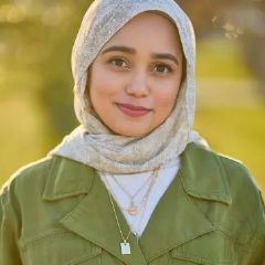 Young woman wearing white hijab and green jacket smiles outdoors