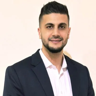 Professional headshot of a man in dark blazer and white shirt against beige background