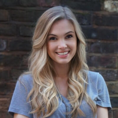 Young woman with blonde wavy hair smiling at camera against brick wall background