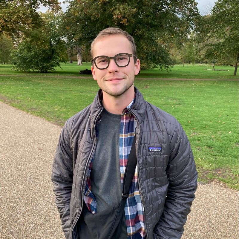 Man wearing glasses and black jacket standing in park pathway