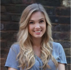 Young woman with long blonde wavy hair smiling at camera wearing blue shirt