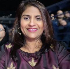Woman with long dark hair wearing purple top and hoop earrings, smiling at camera