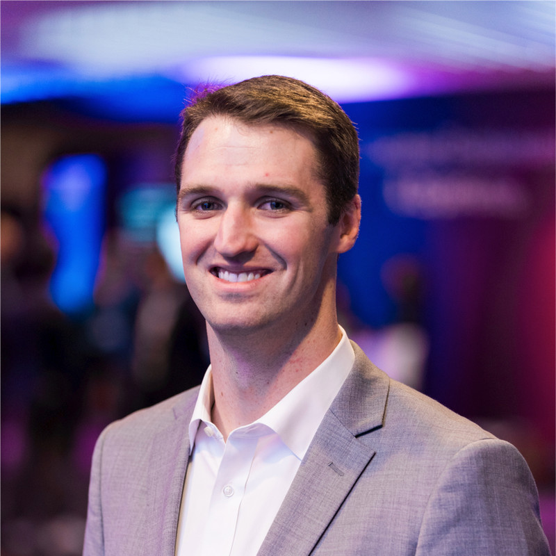 Smiling man in beige blazer and white shirt at colorful nighttime event