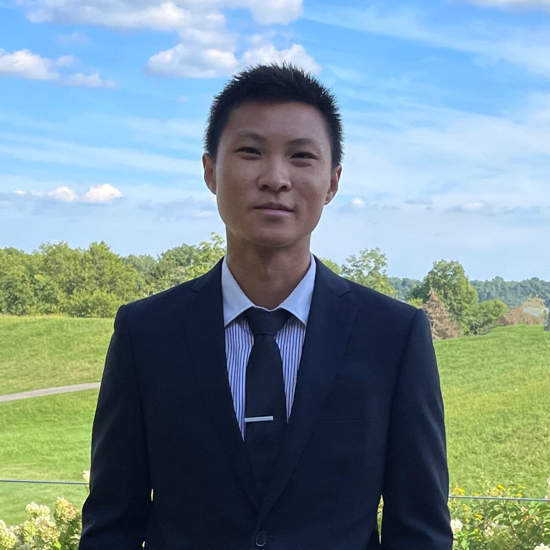 Asian man in dark business suit and blue tie against green field landscape