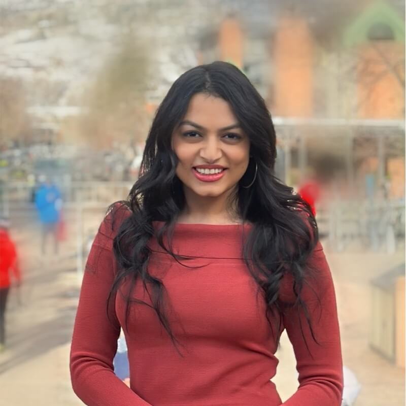 Young woman with long black hair wearing red top smiling outdoors.