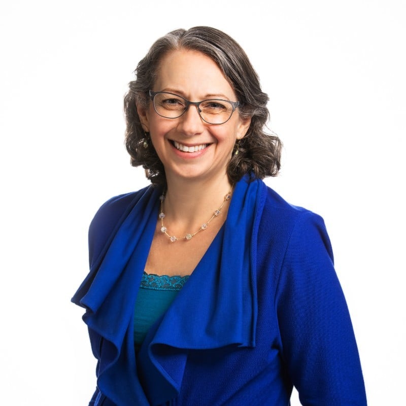 Woman wearing glasses and blue cardigan smiling at camera against white background