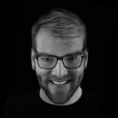Black and white portrait of smiling man wearing glasses against dark background.
