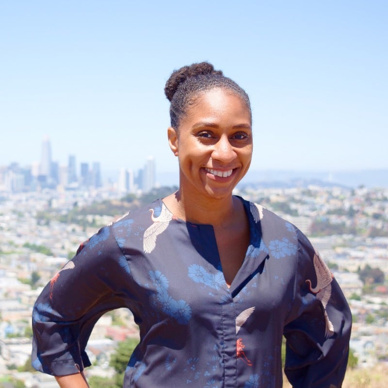 Woman smiling outdoors overlooking city skyline with clear blue sky