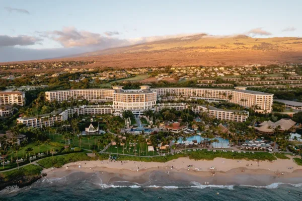 Aerial of Grand Wailea above Wailea Beach at golden hour, with Haleakalā behind