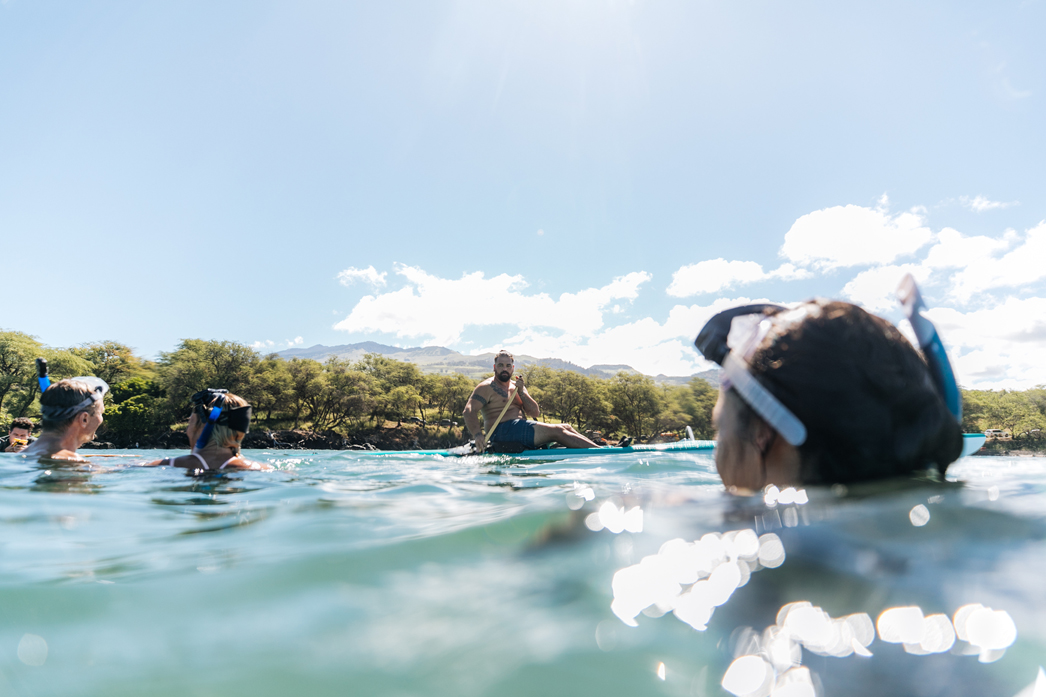A guide instructing a small group of snorkelers floating at the surface near shore