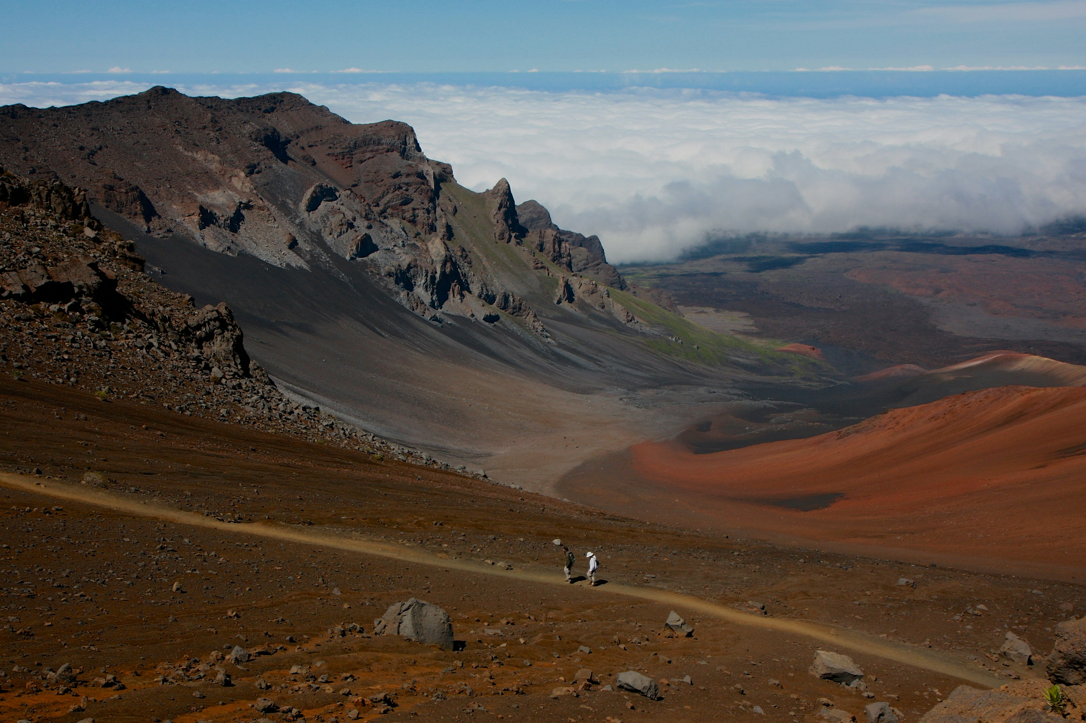 Two hikers on the Haleakala crater trail above a bank of clouds