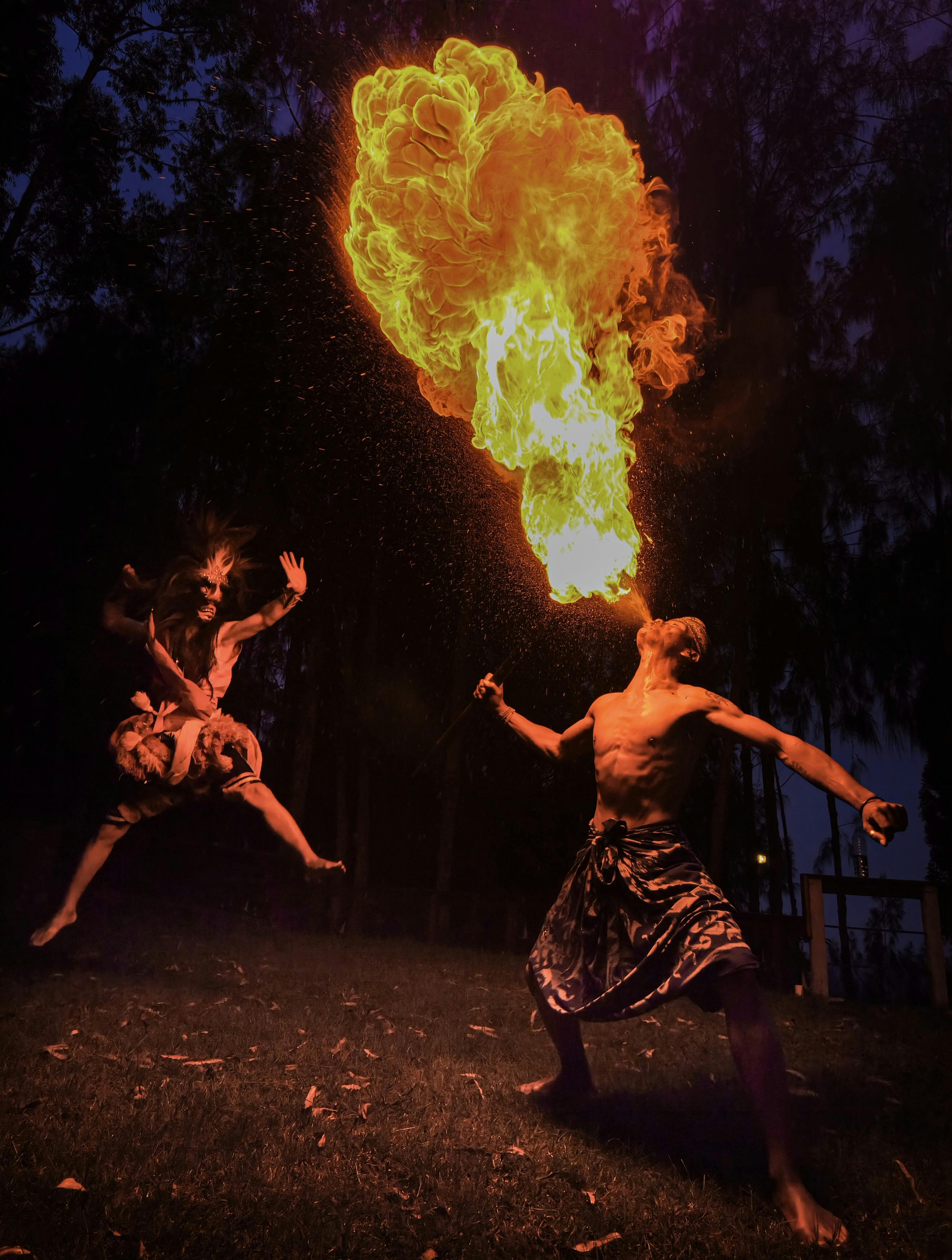 Fire dancer breathing a plume of flame at a nighttime luau performance