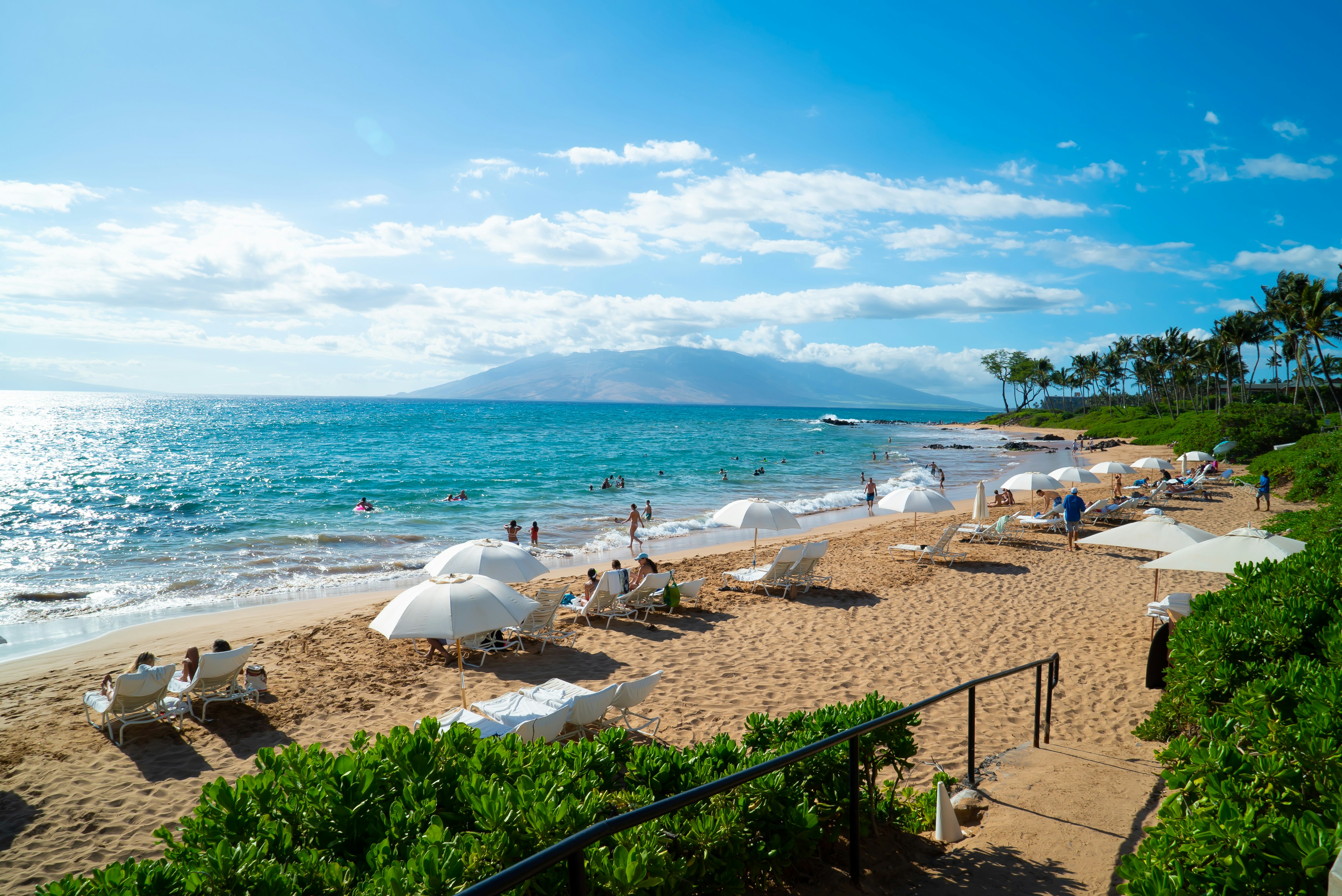 White loungers and umbrellas on the sand at Mokapu Beach in Wailea, with calm turquoise water and mountains across the channel