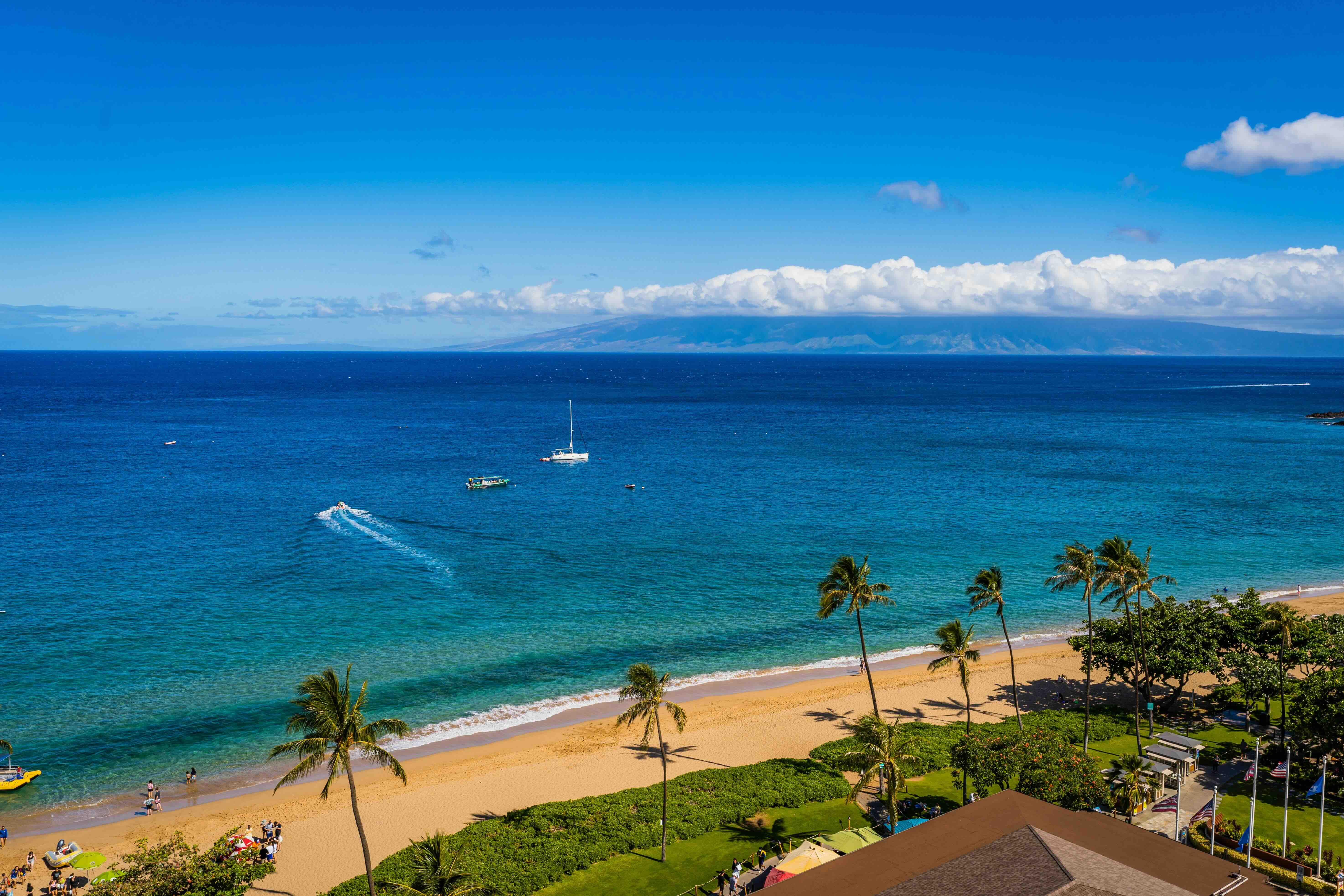 Kāʻanapali Beach seen from above the resort corridor, with catamarans anchored offshore and a neighbouring island across the channel