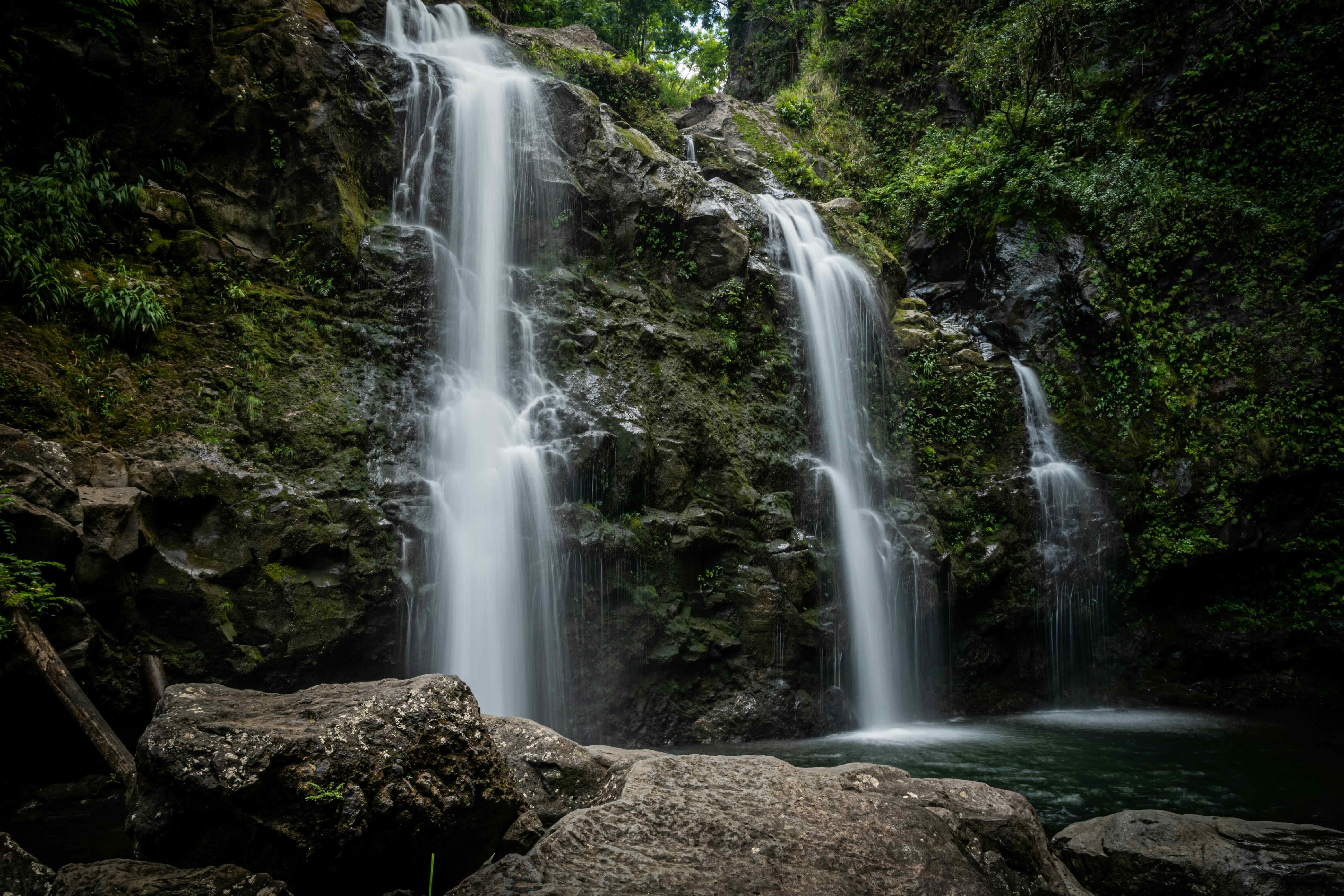 Three waterfalls dropping side by side into a pool surrounded by dark rock and green growth