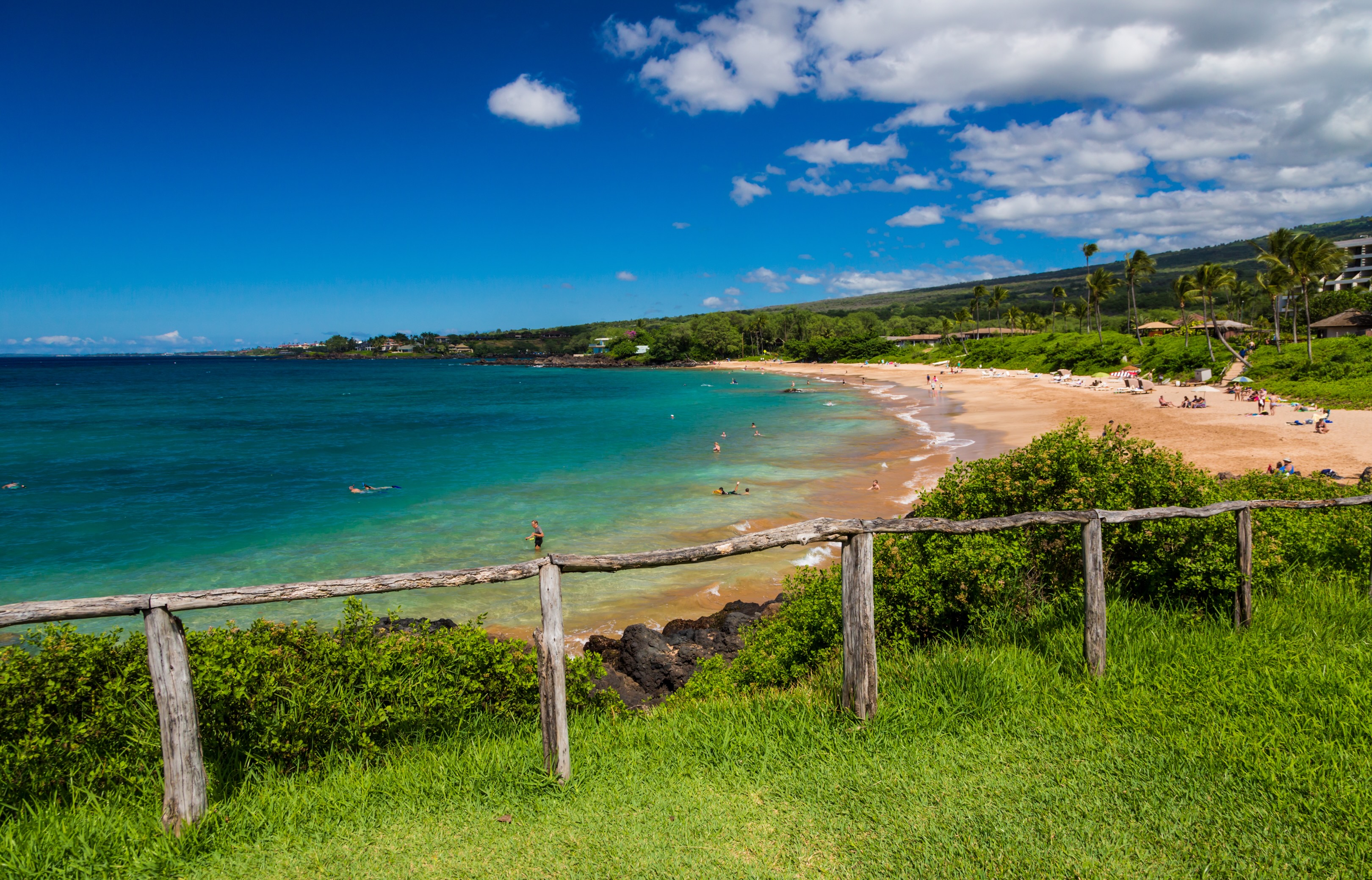 Maluaka Beach at Makena, a sheltered curve of sand seen over a wooden fence and grass