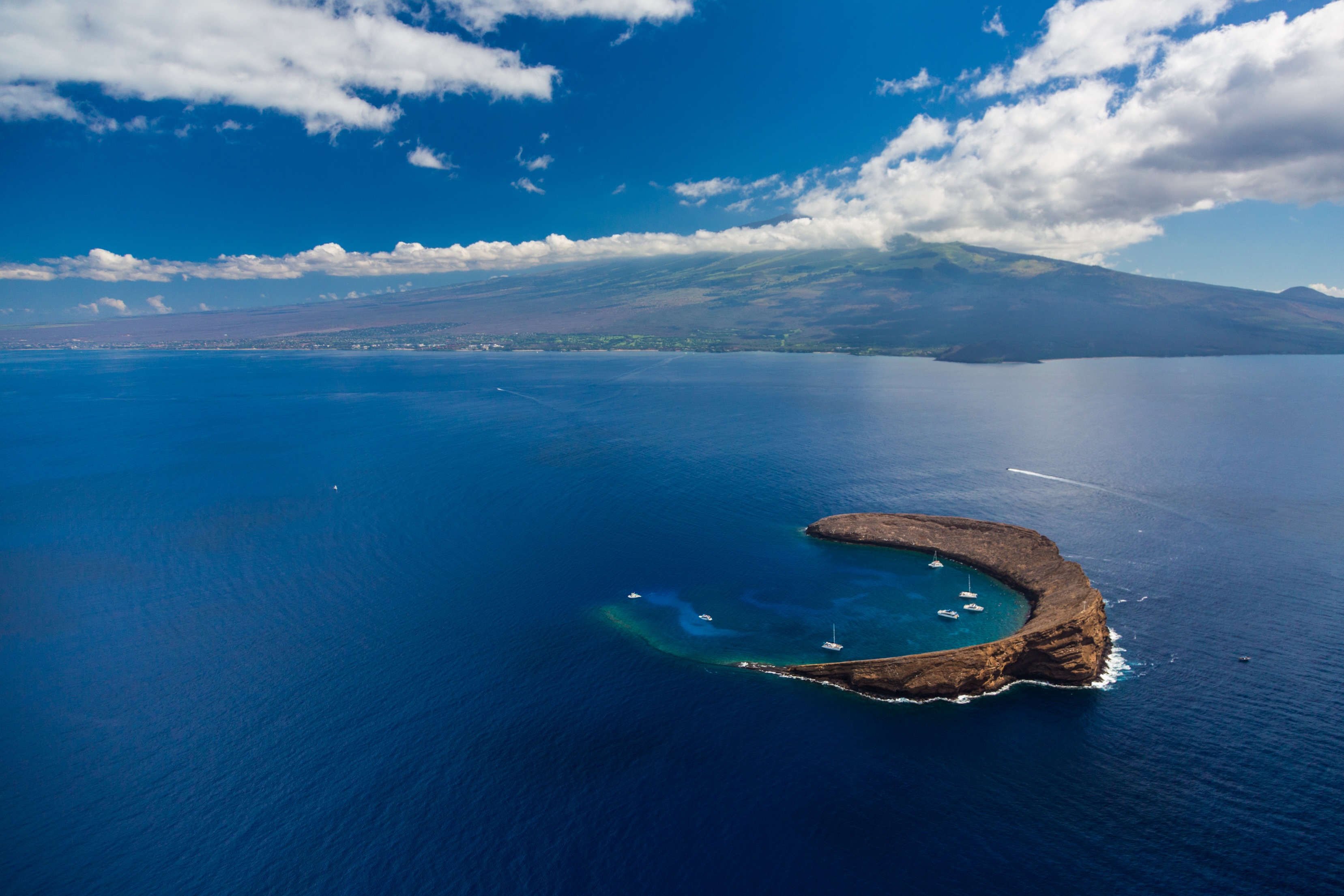 Molokini Crater from the air, a crescent of rock in deep blue water with boats moored inside