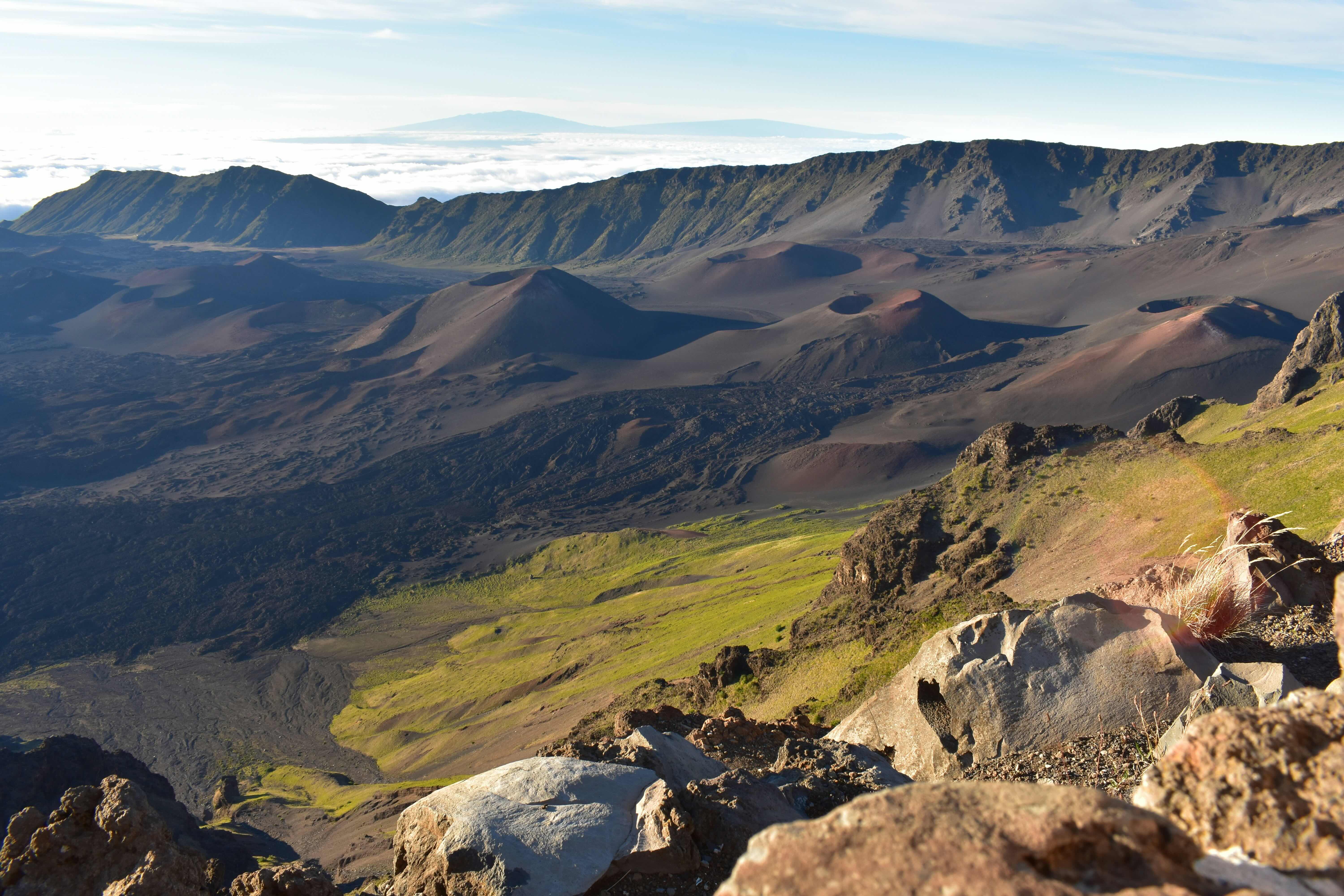 The interior of Haleakala crater in daylight, cinder cones spread across the floor with cloud spilling over the far rim