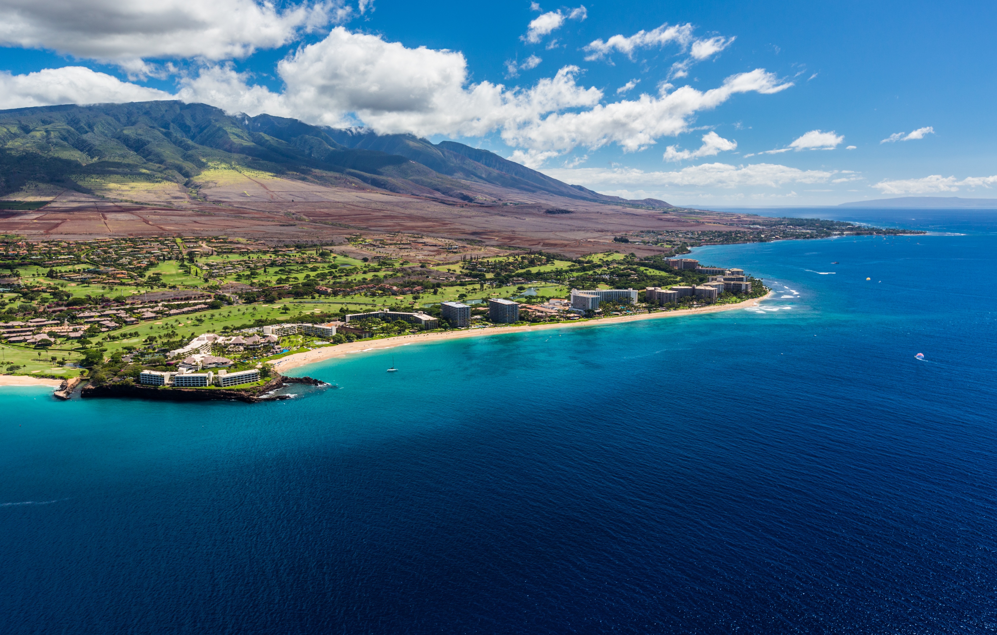 Kaanapali from the air, resorts and golf greens along a long curve of beach with the West Maui Mountains behind