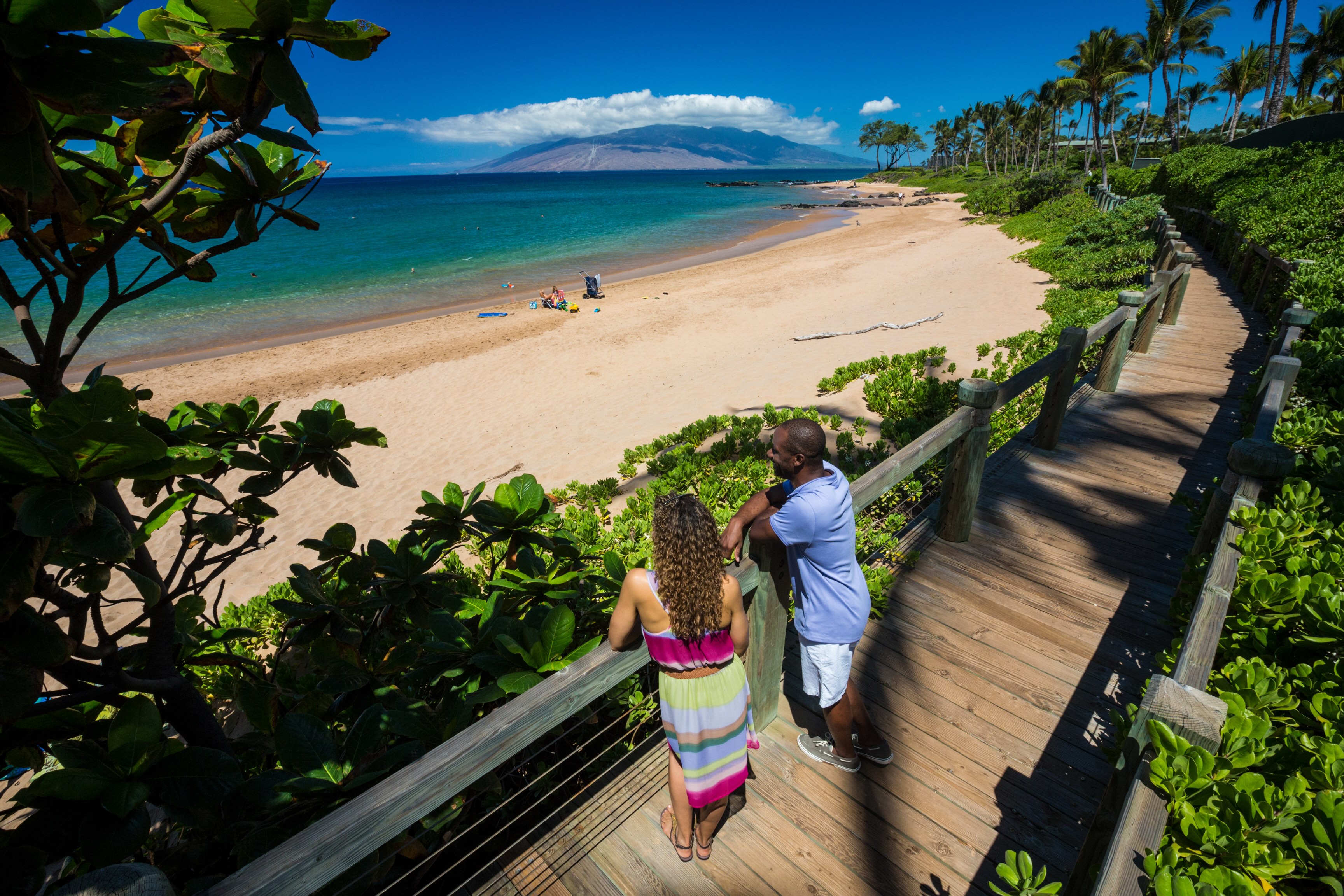 Two people on the wooden Wailea Beach Path looking down at Mokapu Beach, with Kahoolawe across the channel
