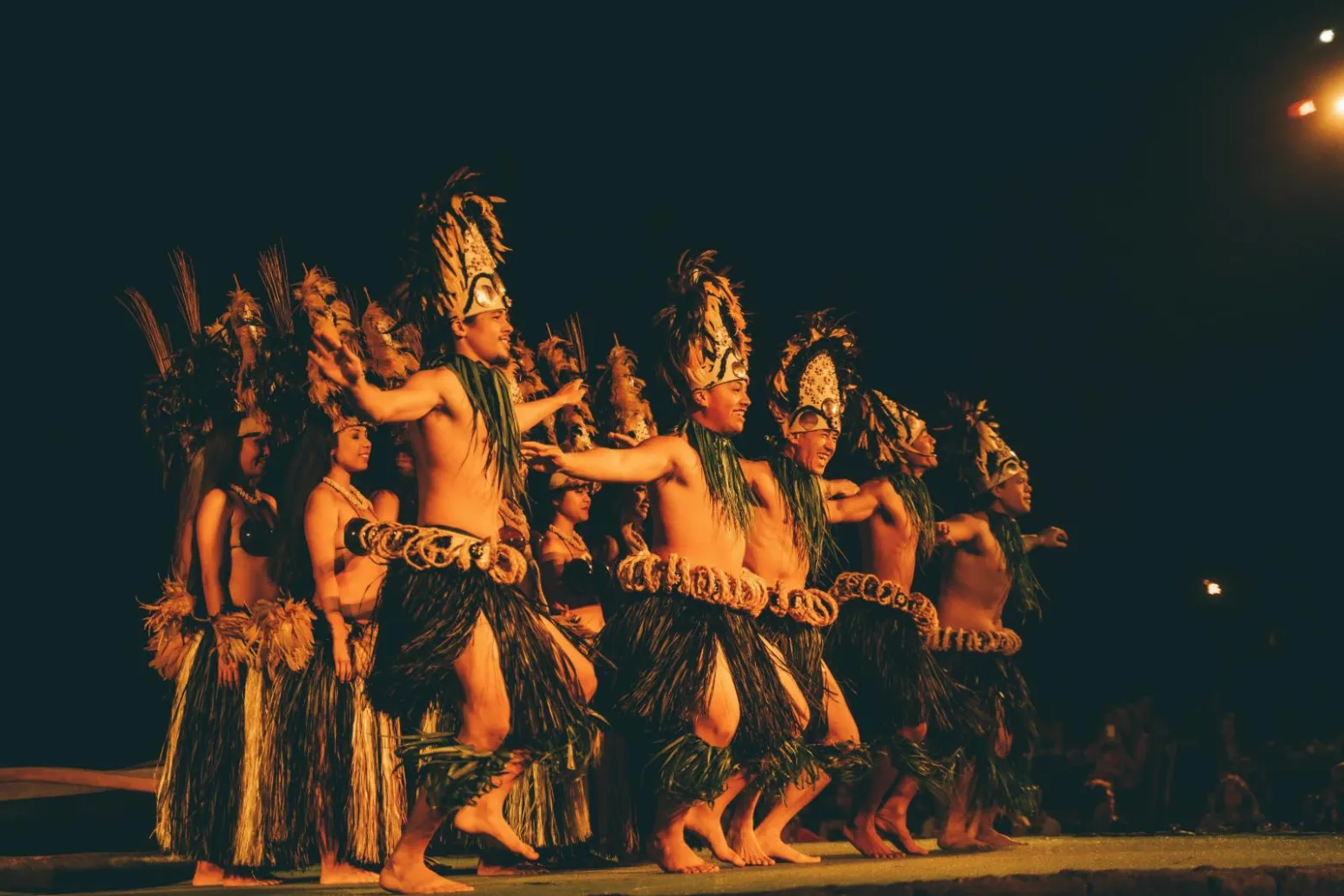 Hula dancers performing in a line on a lit stage at night