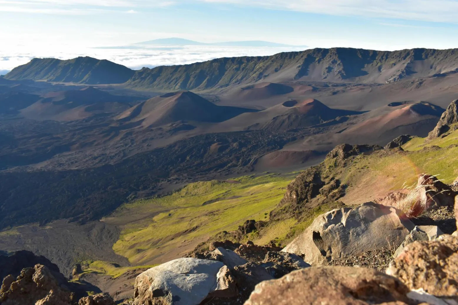 The interior of Haleakala crater in daylight, cinder cones spread across the floor with cloud spilling over the far rim
