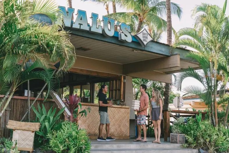 The open-air entrance of Nalu's South Shore Grill in Kīhei, with its sign above and palms around it