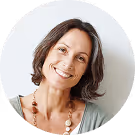 Lächelnde Frau mit braunen Haaren, trägt eine Holzkette, vor weißem Hintergrund.