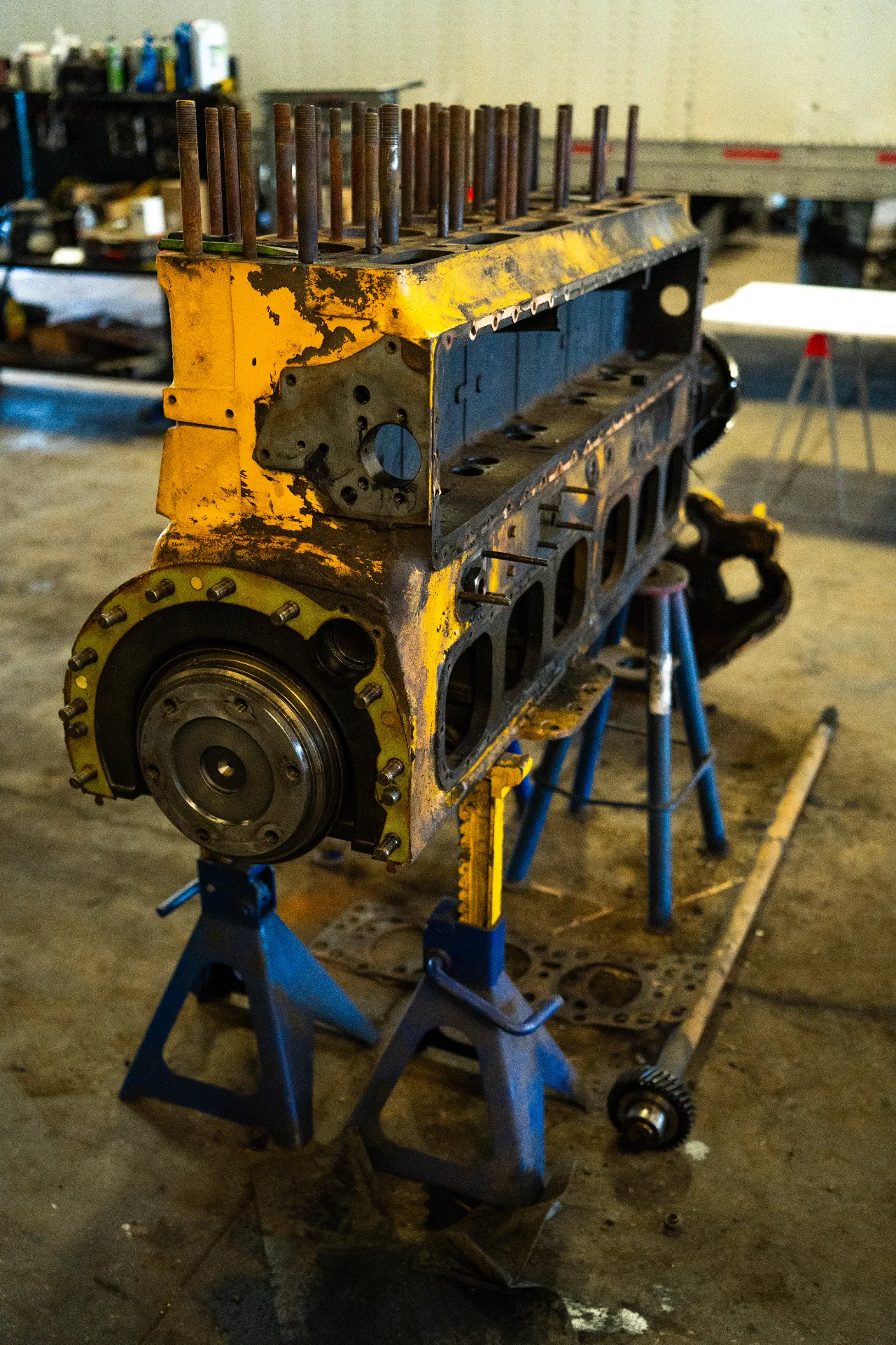 Engine block rebuild on jack stands in a heavy-duty repair shop, with exposed head studs and crank hub.