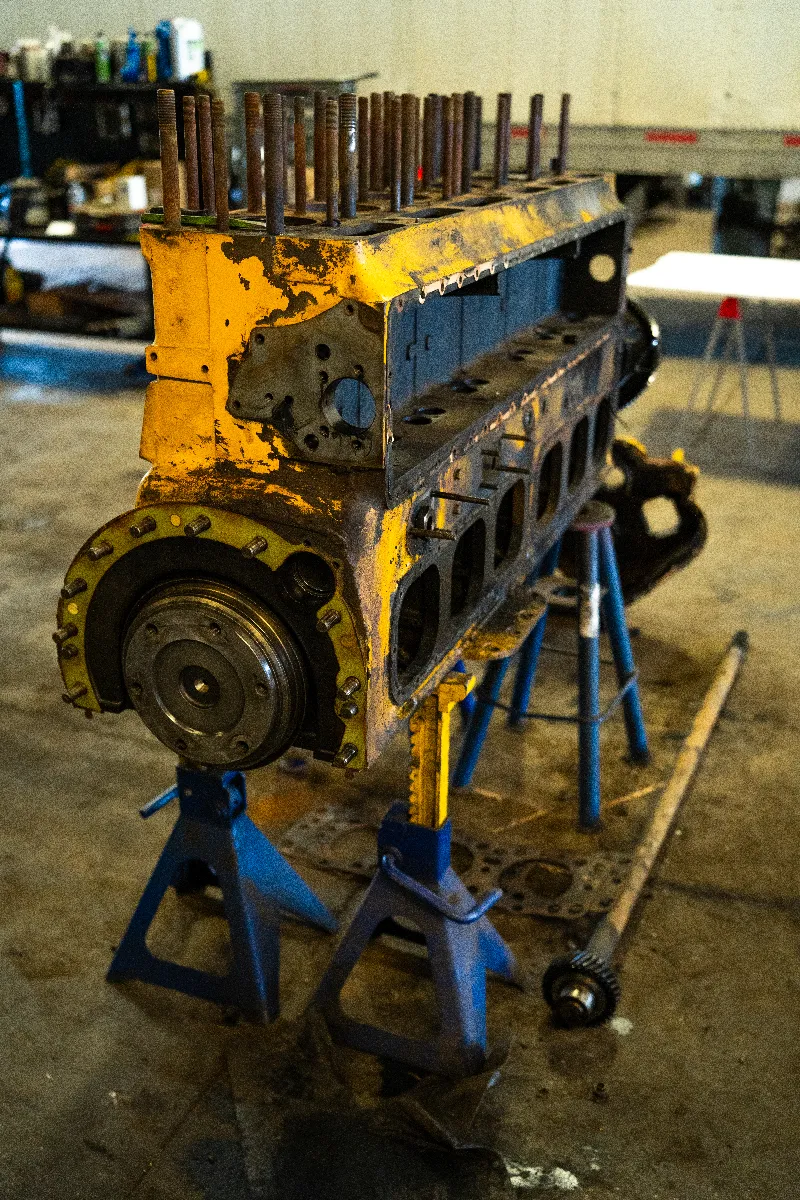 Engine block rebuild on jack stands in a heavy-duty repair shop, with exposed head studs and crank hub.