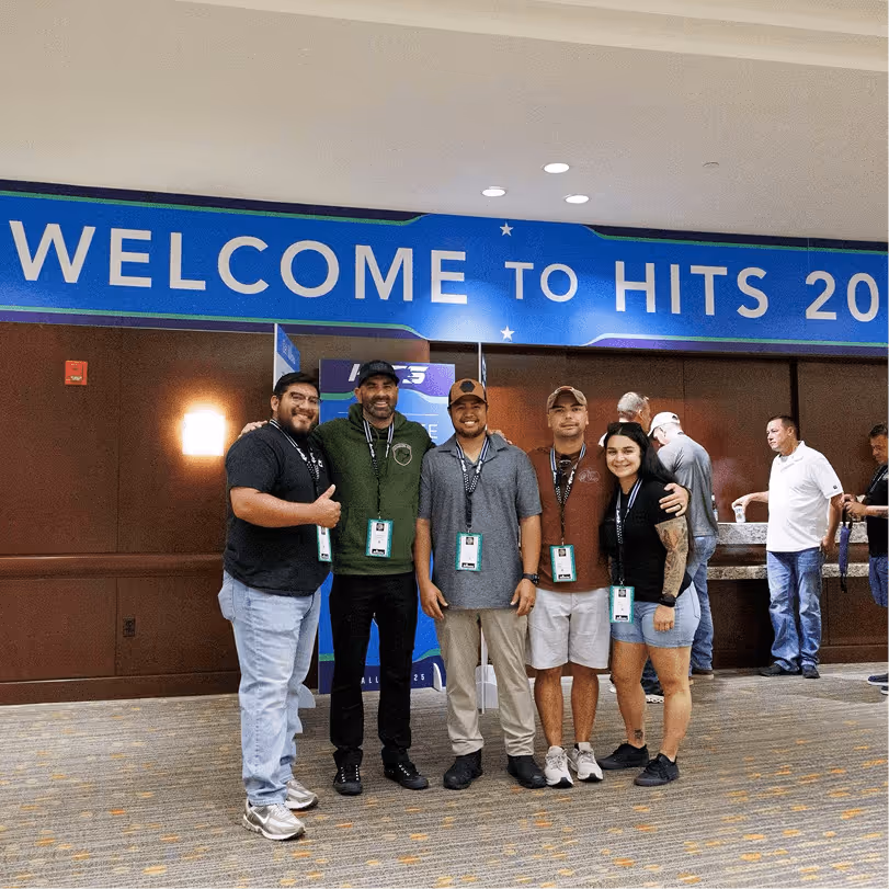Group of five K-9 professionals posing together under the Welcome to HITS banner in the conference lobby