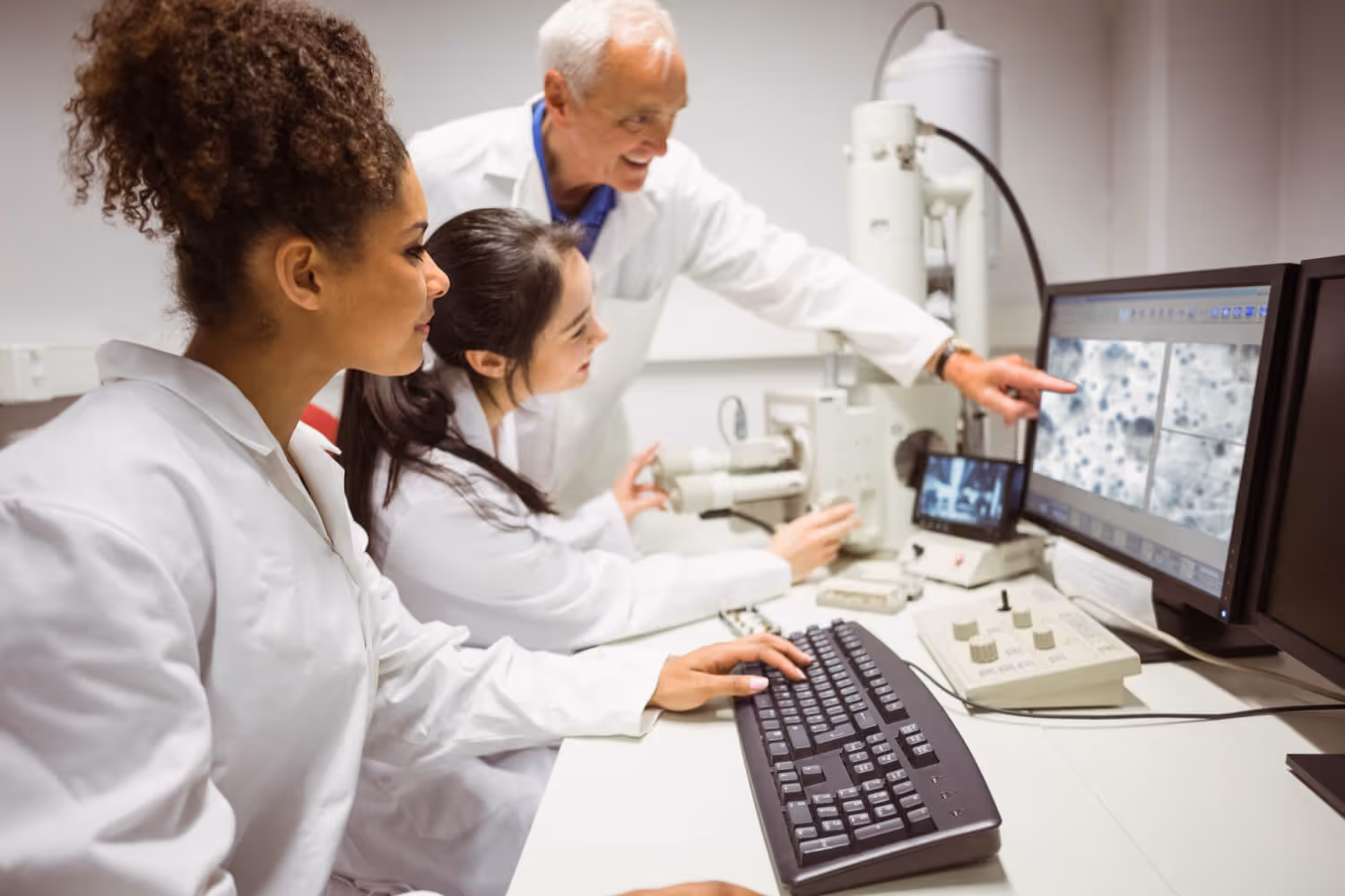 Three scientists in lab coats examining images on a computer screen in a laboratory.