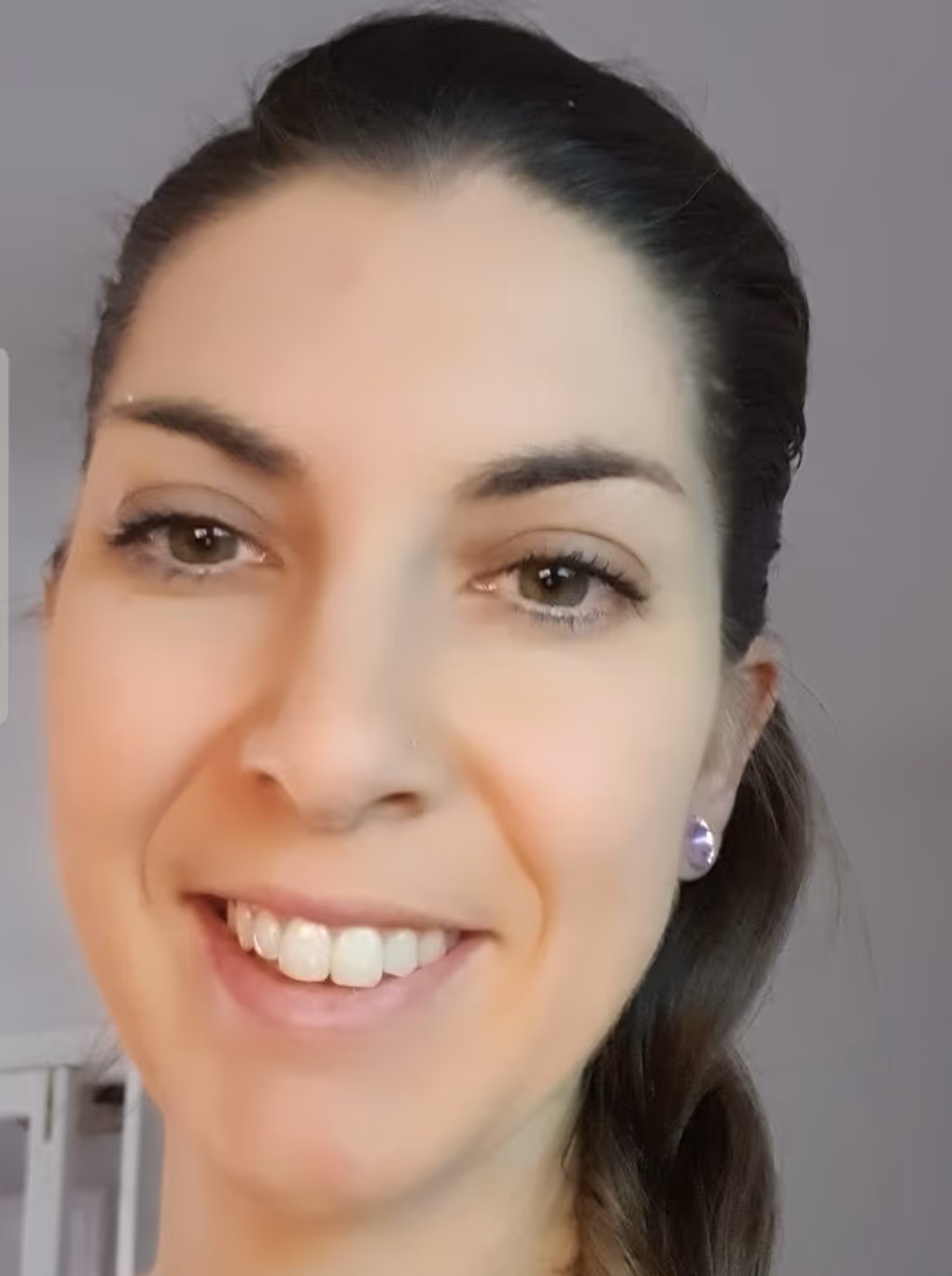 Close-up of a smiling woman with brown hair pulled back and wearing purple stud earrings.